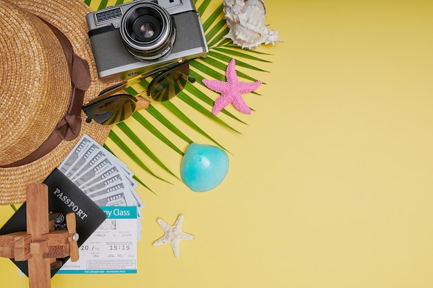 Photo flat lay traveler accessories on yellow background with palm leaf, camera, shoe, hat, passports, money, air tickets, airplanes and sunglasses. top view, travel or vacation concept. summer background.