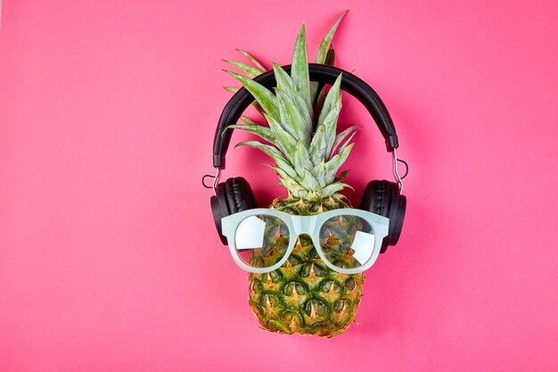 Photo flat lay of trendy, funny face pineapple fruit with headphones and sunglasses.