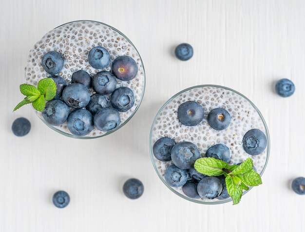 Flat lay of two glasses of organic detox chia seeds pudding dessert with berries topping on table