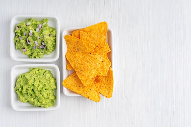 Flat lay of two types of mexican guacamole dipping sauce made of avocado with red onion and nachos