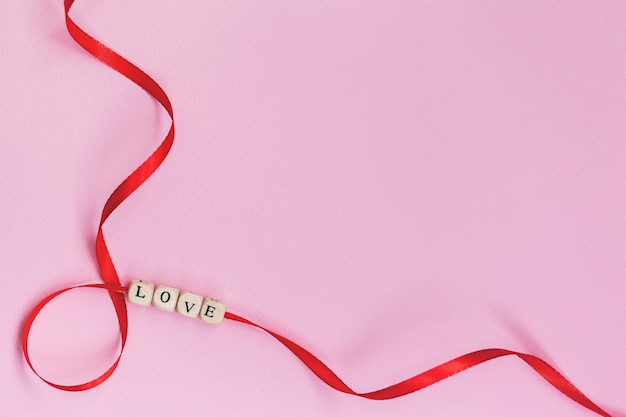 Flat lay Valentines Day concept word Love on red ribbon on pastel pink wall.
