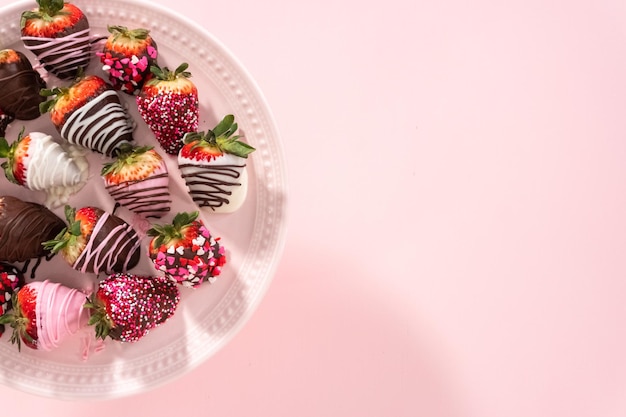 Foto posa piatta varietà di fragole ricoperte di cioccolato su un supporto per torta rosa