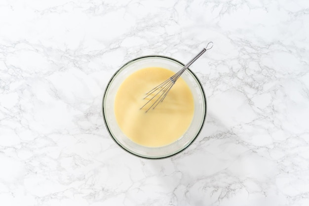 Flat lay Whisking in a large glass bowl together ingredients to make the white chocolate ganache frosting