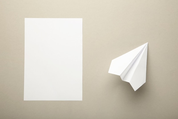 Photo flat lay of white paper plane and blank paper on grey background