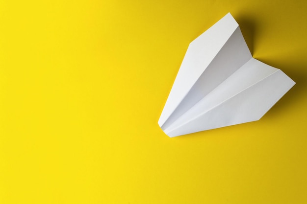 Flat lay of white paper plane and blank paper on pastel yellow color background