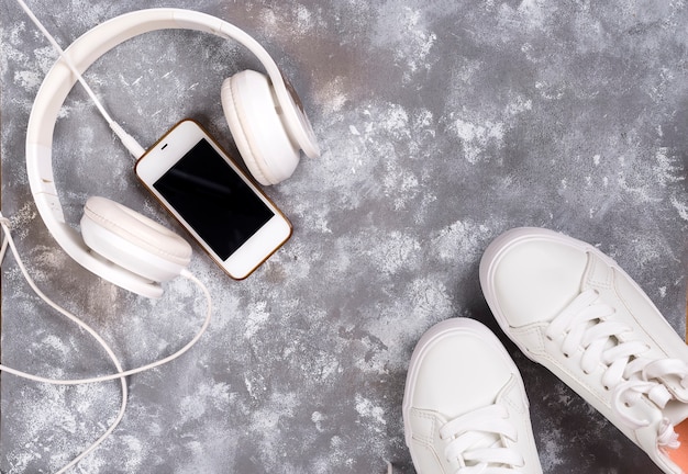 Flat lay Of White Sneakers On stone Background with phone and headphones.