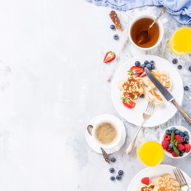 Flat lay with breakfast with scotch pancakes in flower form, berries and honey on light wooden table. Healthy food concept with copy space.