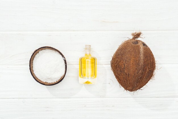 Flat lay with coconut oil in bottle whole coconut and half on white wooden surface