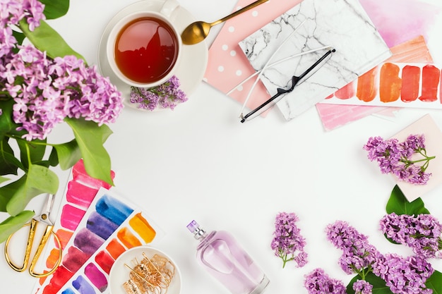 Flat lay with cup of tea, lilac, notebook, and other accessories