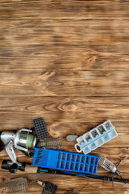 Flat lay with fishing tackle fishing rod and plastic box with
fishing tackle and hooks feeders on wooden planks copy space