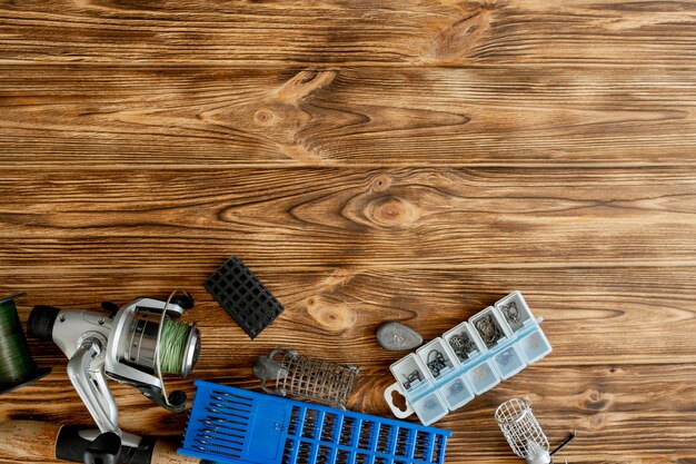 flat lay with fishing tackle, fishing rod and plastic box with fishing tackle and hooks, feeders on wooden planks, copy space