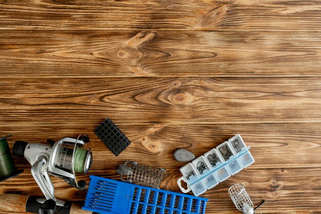 Flat lay with fishing tackle, fishing rod and plastic box with fishing tackle and hooks, feeders on wooden planks, copy space