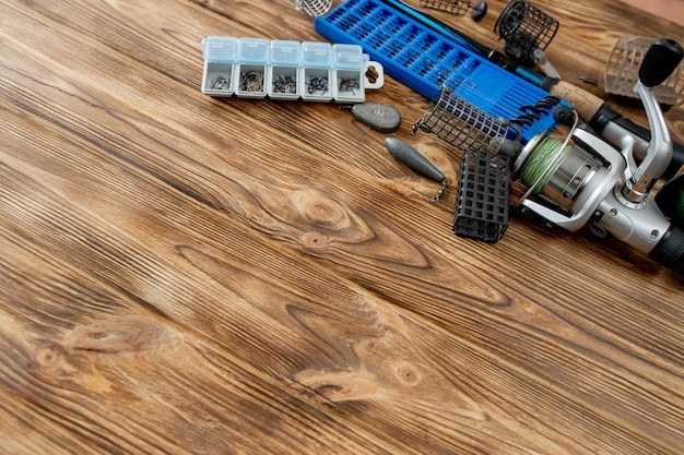 Flat lay with fishing tackle, fishing rod and plastic box with fishing tackle and hooks, feeders on wooden planks, copy space.