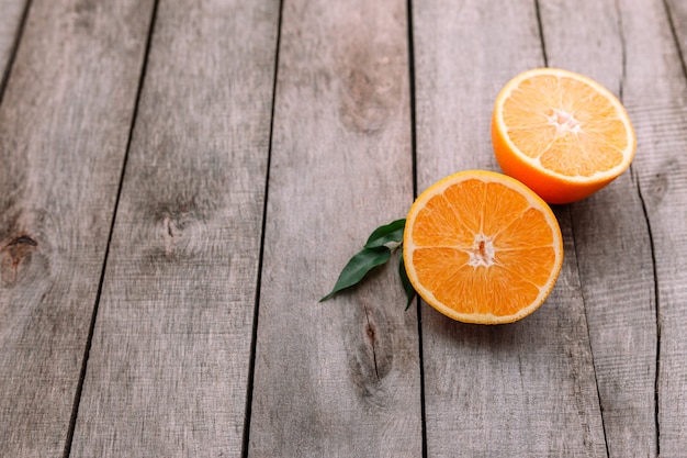 Flat lay with fresh ripe sliced halves of orange fruit on gray wooden table. Orange pulp and green leaves. Tropic food concept. Healthy eating concept.