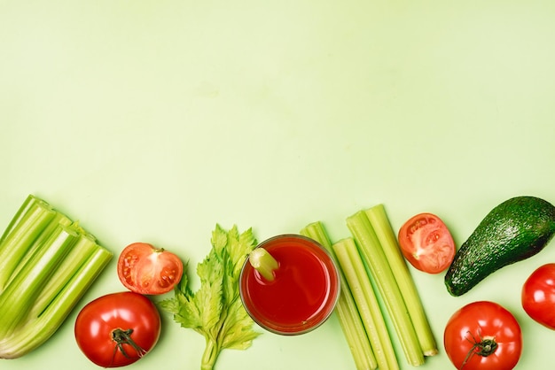 Плоская тарелка со стаканом вкусных и полезных помидоров и соком сельдерея, сырыми помидорами, сельдереем и авокадо