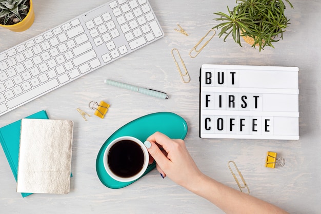 Foto lay piatto con lightbox con testo ma prima caffè e tazza di caffè in mano della donna. social media, blog femminile, mattina del concetto di giornata lavorativa. vista dall'alto