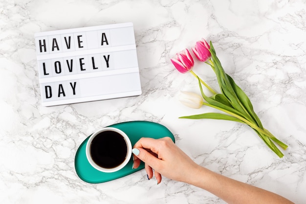 Foto lay piatto con lightbox con testo buona giornata e tazza di caffè in mano alla donna. social media, citazione di motivazione, blog femminile, concetto di mattina del giorno lavorativo