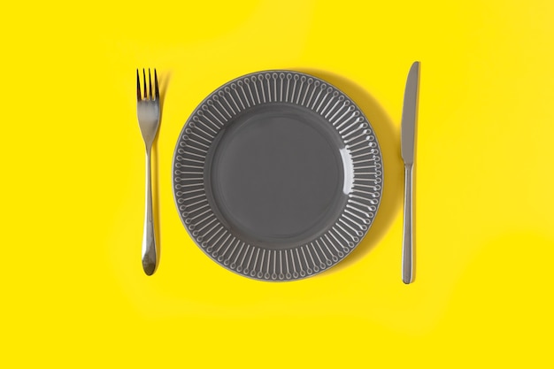 Flat lay with mock up gray plate and cutlery on trendy yellow background with copy space