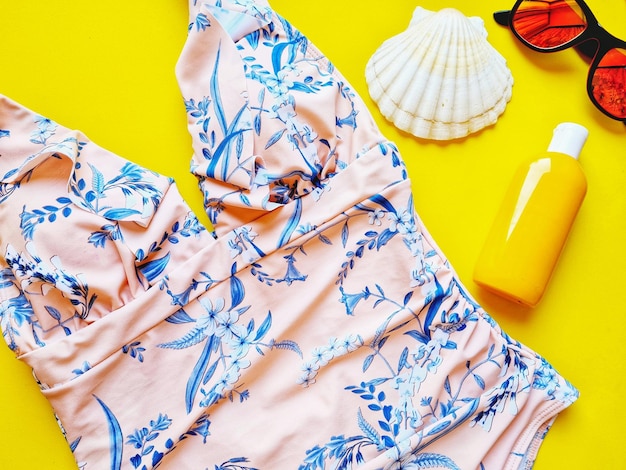 Flat lay with pink one piece swimsuit sunglasses and sunscreen on yellow background