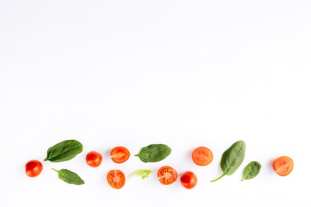 Flat lay with red cherry tomatoes and green spinach leaves on a white background. Healthy eating concept