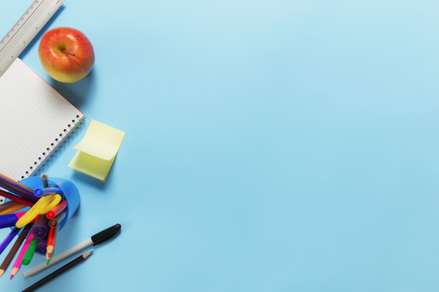 Flat lay with school, education or work desk concept with various schooling accessories, pens, pencil, notepad, paper clips, apple, ruler, scissors, paper sticker on blue surface