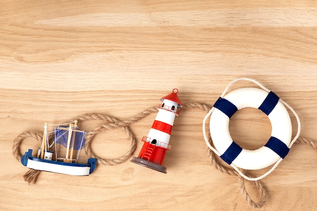 Foto lay piatto con vacanze estive in simboli lato mare. faro, barca, corda da marinaio. copia spazio, vista dall'alto