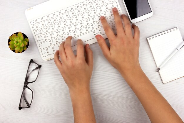 Flat lay with white keyboard, cactus, glasses and hands