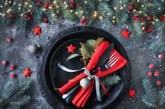 Flat lay with Xmas decorations in green and red with frosted berries, trinkets, black plates and crockery