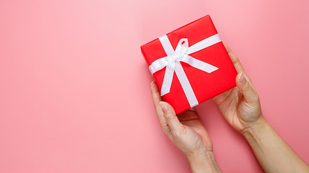 Flat lay of woman hands holding gift wrapped and decorated with bow isolated on pink background with copy space. Valentines love. Birthday theme.