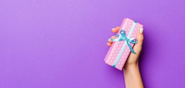 Flat lay of woman hands holding gift wrapped and decorated with bow on purple background