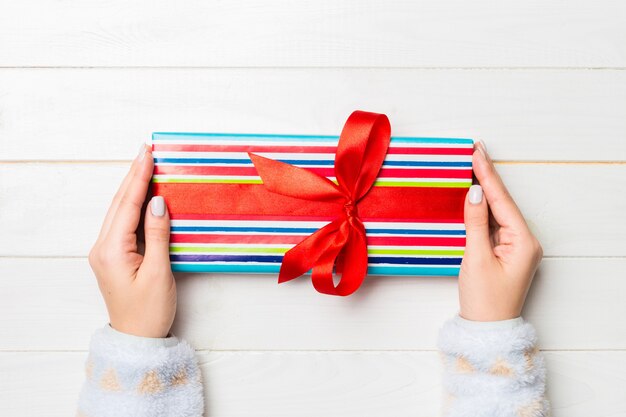 Disposizione piana delle mani della donna che tengono regalo avvolto e decorato con l'arco su fondo di legno bianco con lo spazio della copia. natale e concetto di vacanza.