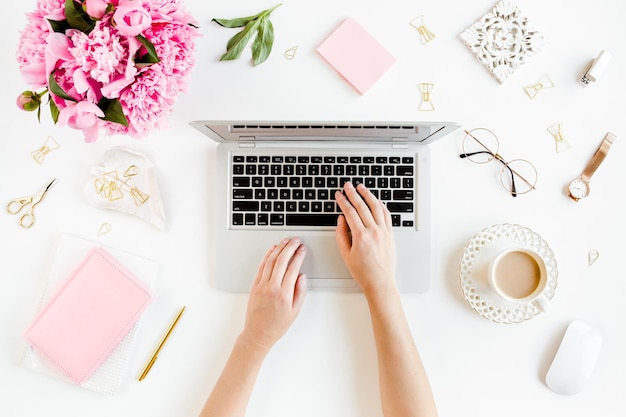 Flat lay women's office desk Female workspace with laptop pink peonies bouquet