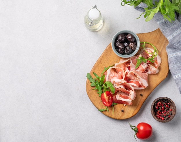 Flat lay of a wooden board with bacon or prosciutto on a light background