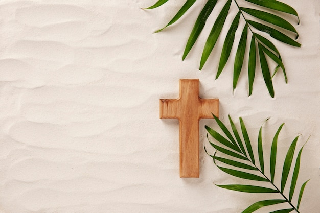 Flat lay wooden cross and leaves on sand