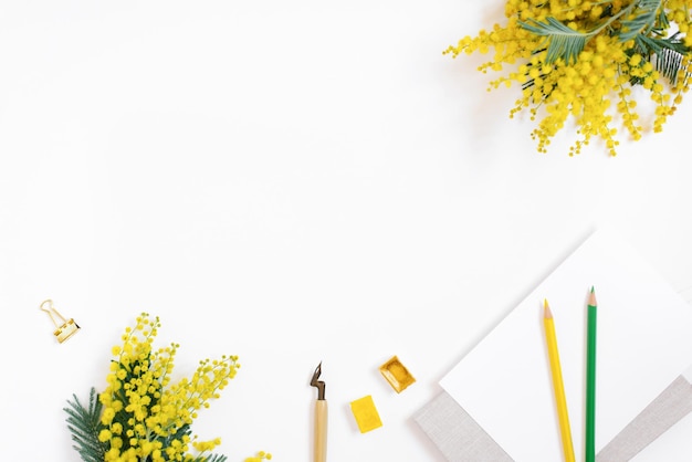 Flat lay of the workplace of a calligrapher blogger A sheet of paper a pen for calligraphy colored pencils flowers watercolor paints on a white background with a copy space