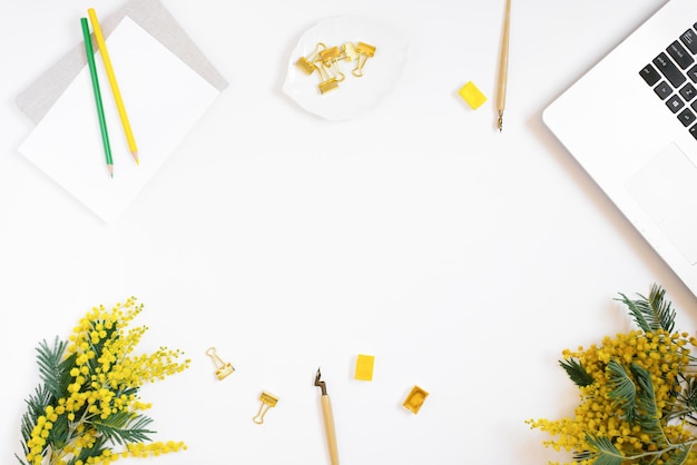 Flat lay of the workplace of a calligrapher blogger A sheet of paper a pen for calligraphy colored pencils notebook flowers watercolor paints on a white background with copy space