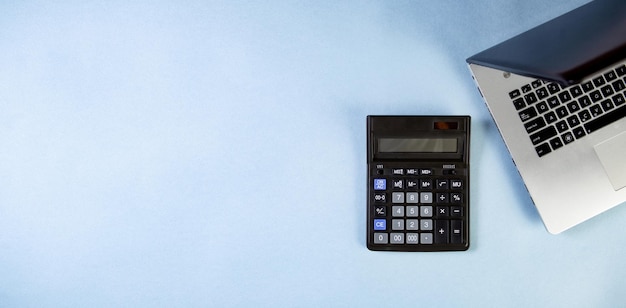 Flat lay of workspace with calculator and laptop on the blue background. Place for text.