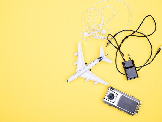 Flat lay on yellow background of plane top view next to headphones ,battery charger and camera