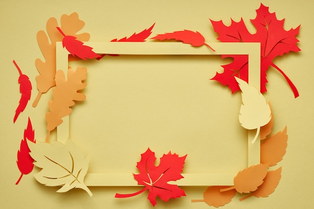 Flat lay on yellow paper, paper frame with red and orange Autumn leaves