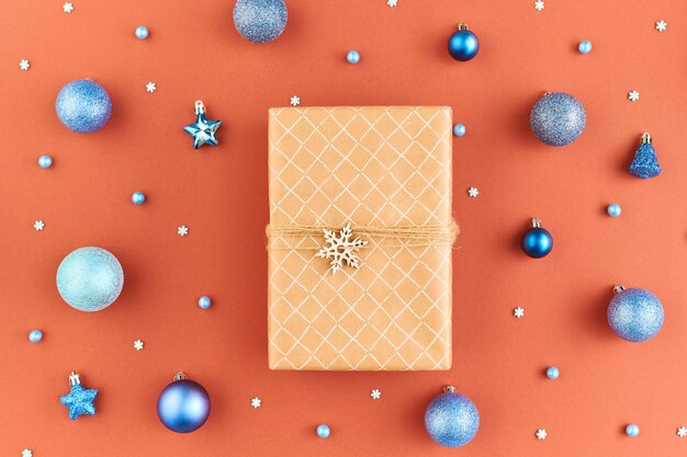 Flat layout of box with Christmas gift with wooden decoration on top surrounded by group of snowflakes, blue and silver toy balls and stars