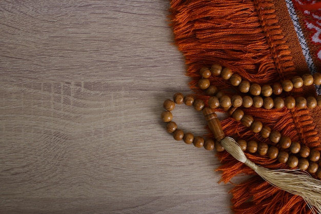 木製の背景のイスラムの概念上の数珠と祈りの敷物のフラットレイアウト
