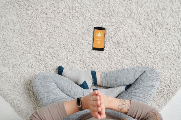 Flat layout of young woman with crossed legs keeping hands together by chest while meditating on the floor