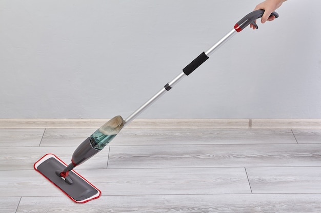 Flat mop with spray and microfiber head is cleaning laminate\
floor in room from dust and dirt.