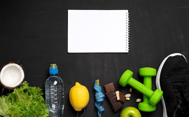 Flat photo of sports equipment - dumbbells, table tennis\
rackets, tape measure, exercise equipment, water bottle and fruit,\
protein bars and a white tablet on a dark background for your\
recording.