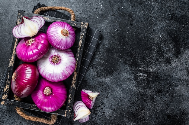 Photo flat red sweet onion in a wooden tray. black table. top view.