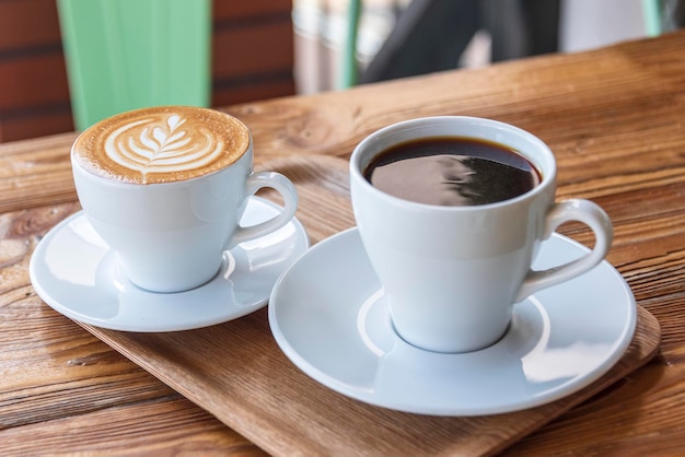 フラットホワイトまたはカプチーノと木製のテーブルの上の白いカップのフィルターコーヒー小さな木製のトレイのカフェでさまざまなコーヒースタイルの朝の飲み物