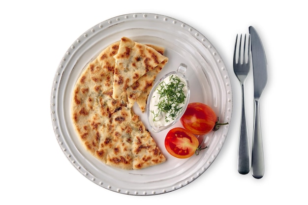 Flatbread with cheese and herbs and yoghurt sauce on a white plate with cutlery decorated with tomatoes Mediterranean food Top view flat lay