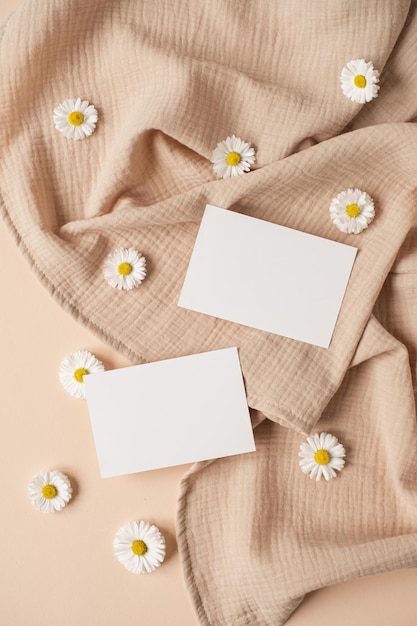 Flatlay of aesthetic Parisian styled business branding template Blank paper sheet card with mockup copy space chamomile flower buds and muslin cloth on neutral beige background Flat lay top view