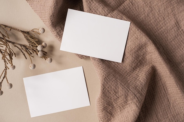 Foto flatlay del modello di branding aziendale in stile parigino estetico scheda di foglio di carta bianca con spazio di copia mockup ramo di fiori secchi e panno su sfondo beige neutro vista dall'alto piatta