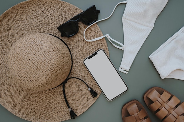 Flatlay of aesthetic women's fashion accessories Mobile phone with blank copy space screen Stylish female straw hat swimsuit sunglasses sandals on pastel background Top view flat lay